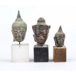 3 small Buddha heads, Southeast Asia, 19th century and earlier, bronze. 2 x mounted on wooden, 1 x