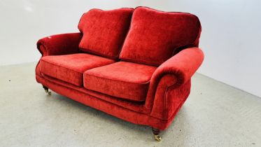 MODERN RED UPHOLSTERED TWO SEAT SOFA ON BRASS CASTORS.