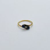 AN 18CT GOLD CROSS OVER RING SET WITH A CENTRAL DIAMOND & 2 SAPPHIRES.