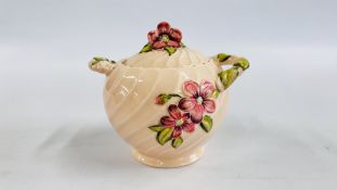 A CLARICE CLIFF NEWPORT POTTERY GLAZED TWO HANDLED POT AND COVER WITH RAISED FLOWERS ON A PALE PINK