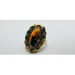 A YELLOW METAL (WORN MARKS) OVAL AMBER TYPE SET RING IN FILIGREE MOUNT - SIZE L/M.