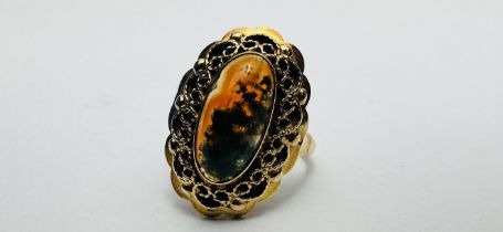 A YELLOW METAL (WORN MARKS) OVAL AMBER TYPE SET RING IN FILIGREE MOUNT - SIZE L/M.