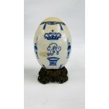 A CONTINENTAL PORCELAIN COMMEMORATIVE EGG ON AN ELABORATE BRASS BASE - H 19CM.