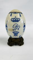 A CONTINENTAL PORCELAIN COMMEMORATIVE EGG ON AN ELABORATE BRASS BASE - H 19CM.