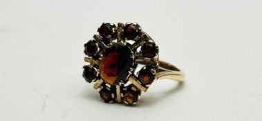 A 9CT GOLD GARNET SET FLOWER HEAD RING - SIZE L/M.