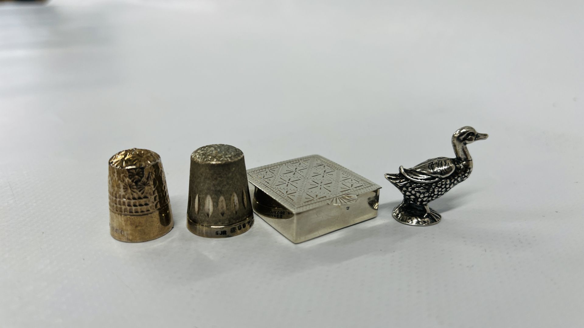 A SOLID SILVER DUCK, SILVER ENGRAVED PILL BOX AND 2 SILVER THIMBLES.
