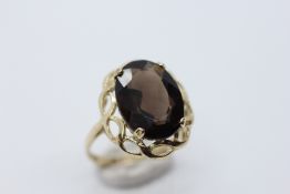 A 9CT GOLD RING SET WITH A SMOKY QUARTZ IN AN ORNATE OVAL RAISED SETTING.