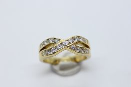 AN IMPRESSIVE YELLOW METAL (RUBBED MARKS) CROSS OVER RING SET WITH 17 DIAMONDS.