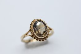 A 9CT GOLD RING SET WITH A SMOKY QUARTZ IN AN ORNATE OVAL SETTING.