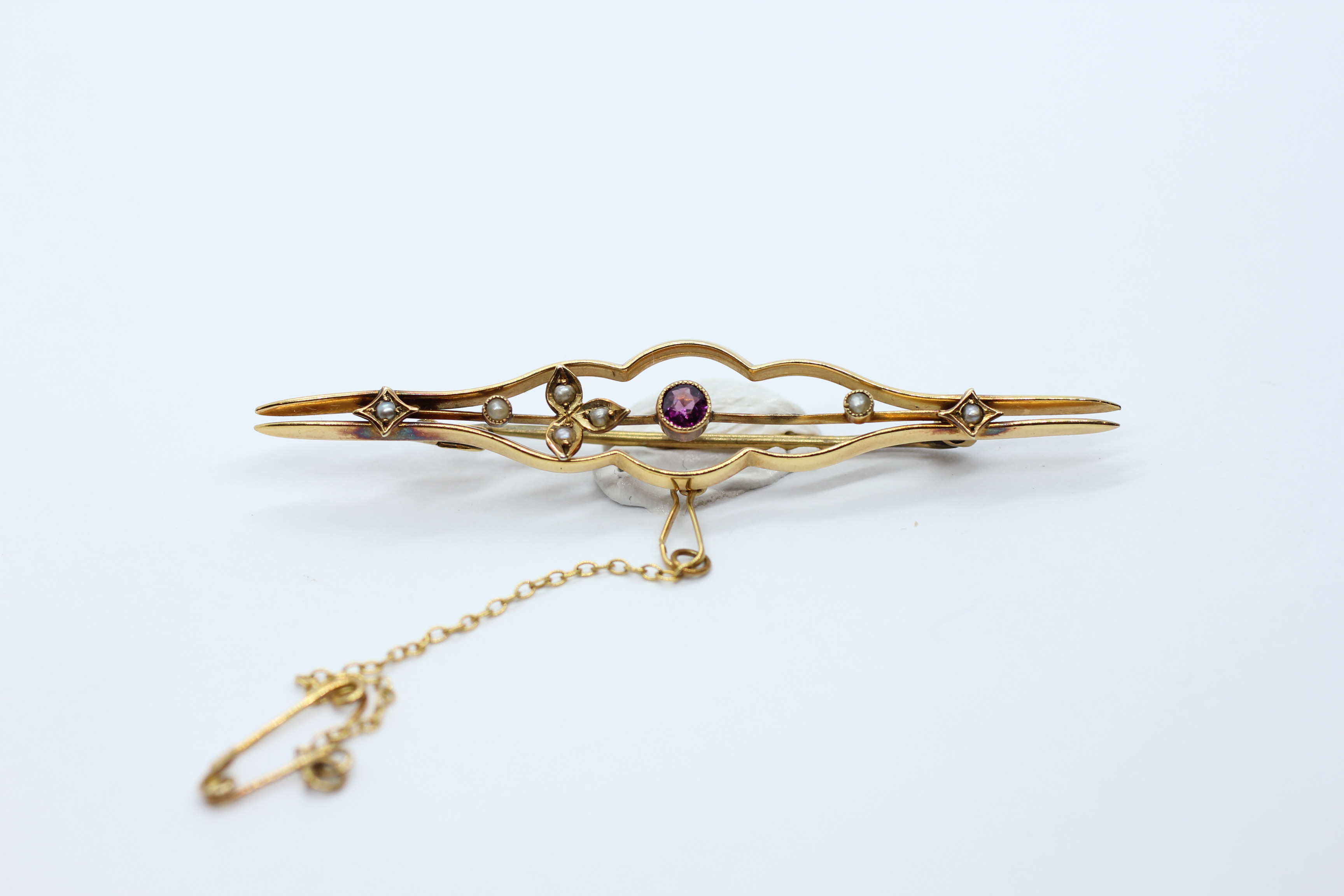 A VINTAGE 9CT GOLD BAR BROOCH AND SAFETY CHAIN SET WITH A CENTRAL AMETHYST AND SEED PEARLS - L 6.