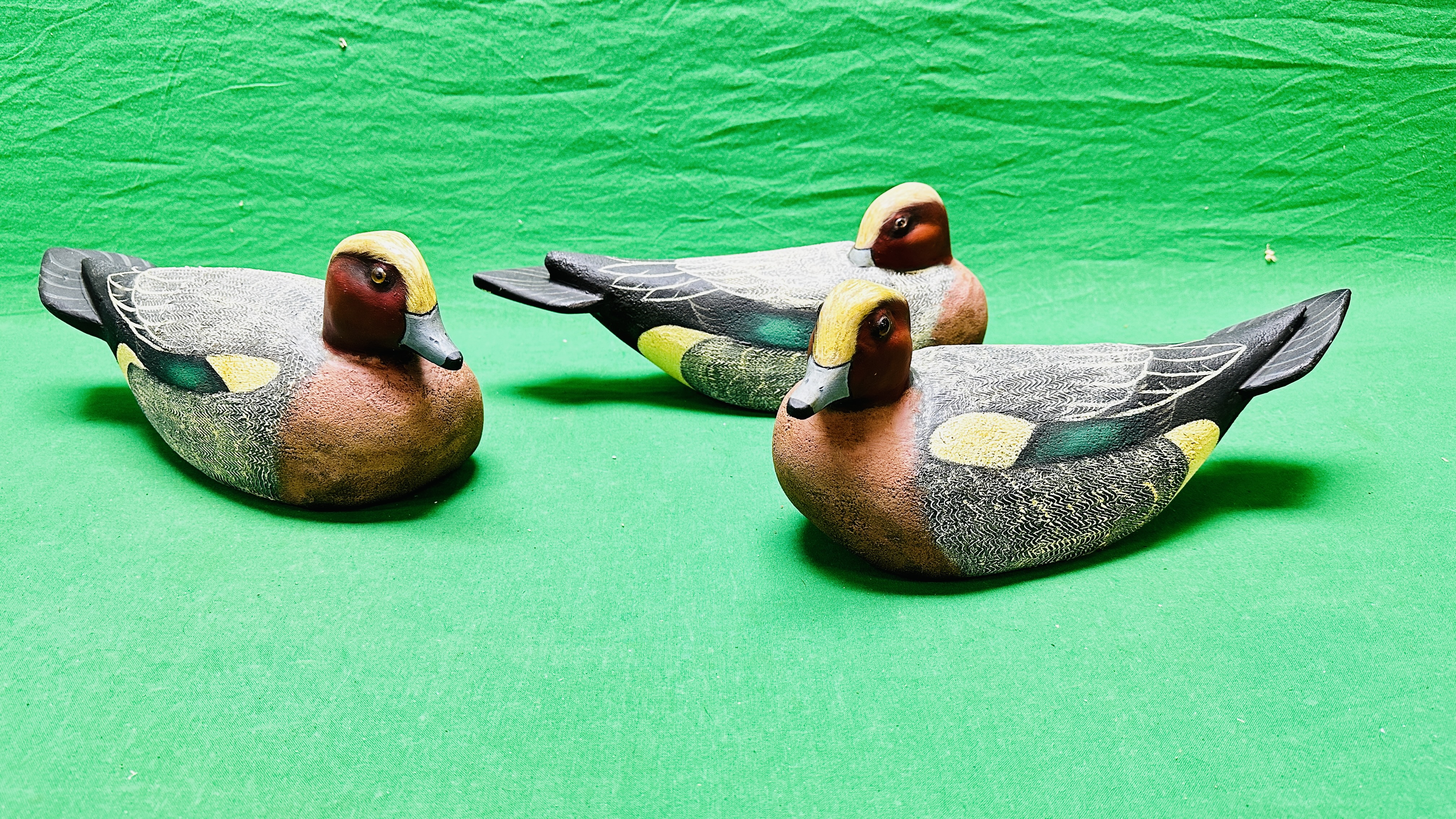 A HANDCRAFTED SET OF THREE DUCK DECOYS HAVING HANDPAINTED DETAIL AND GLASS EYES.