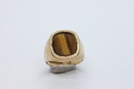A 9CT GOLD GENTS SIGNET RING INSET WITH A POLISHED TIGERS EYE PANEL.