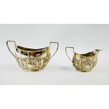 AN EDWARDIAN SILVER EMBOSSED TWO HANDLED SUGAR BOWL AND CREAM JUG,