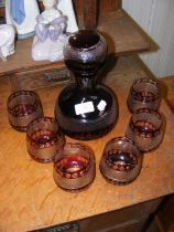 A red glass decanter with six matching glasses