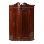 A 19TH CENTURY MAHOGANY SERPENTINE FRONTED HANGING CORNER CUPBOARD IN THE MANNER OF DUNCAN PHYFE