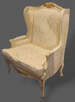 A French cream painted wingback armchair with carved gilded decoration raised upon shaped feet