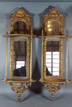 A pair of gilded wall brackets, each with a mirrored back of arched form, 70cms tall