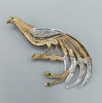 A 9ct gold brooch in the form of a peacock upon a branch, set with diamond and emeralds, 4cms long