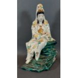 A Japanese porcelain figure in the form of Guan Yin holding a scroll upon green glazed rocky base,