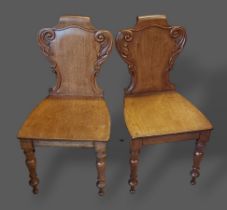 A pair of Victorian mahogany hall chairs, the carved backs above panel seats raised upon turned legs