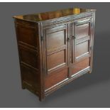 A George III oak bacon cupboard with a carved frieze above two moulded doors flanked by stiles,