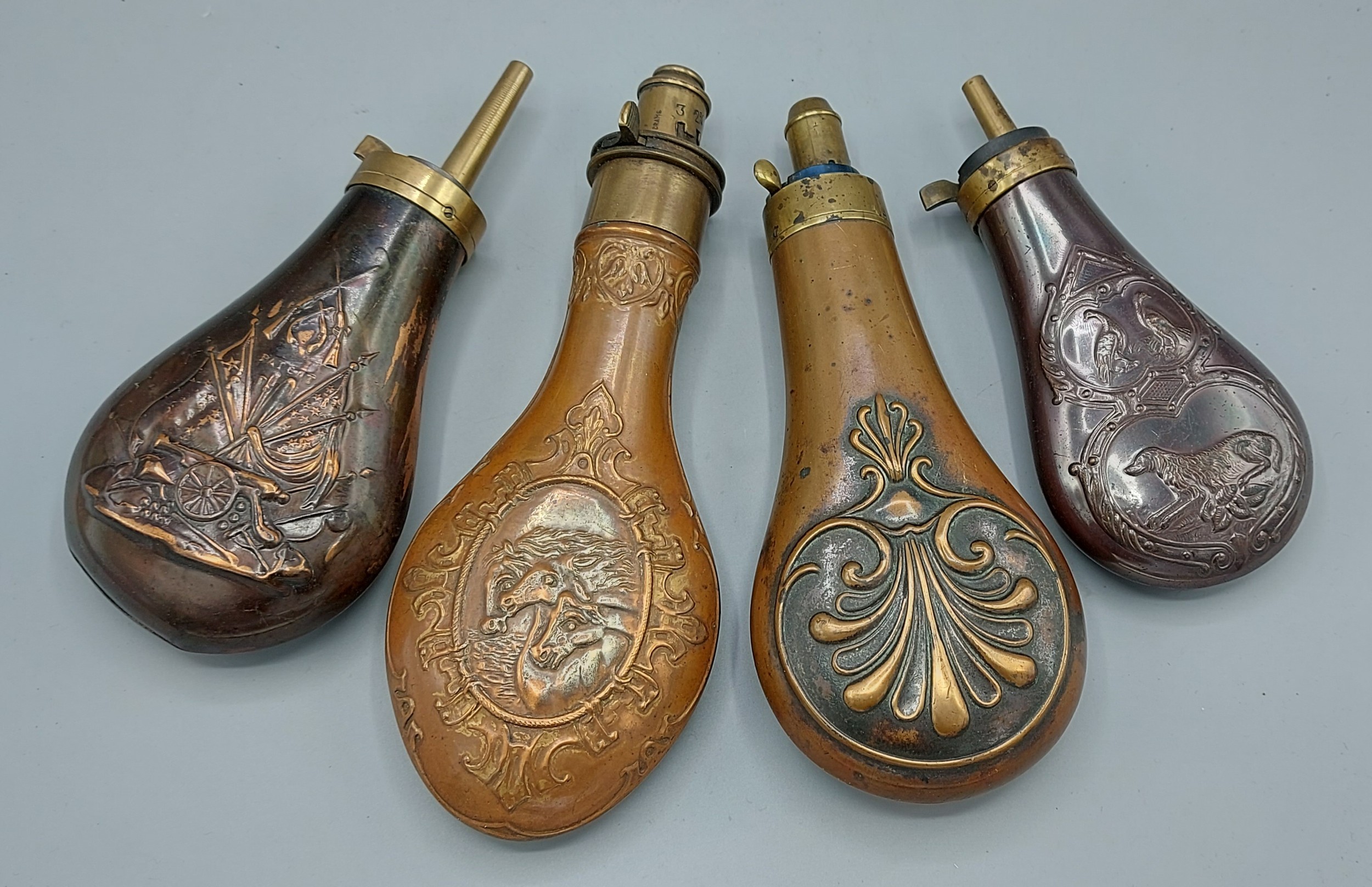A group of four early metal powder flasks, one decorated with an Artillery cannon