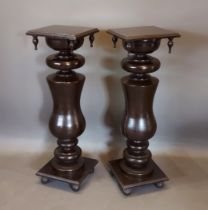 A Pair of ebonised torchere, each with a square moulded top above a turned column and raised upon