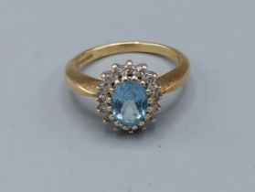 An 18ct gold ring set with a central Aquamarine surrounded by Diamonds, claw set, 3.7gms, ring