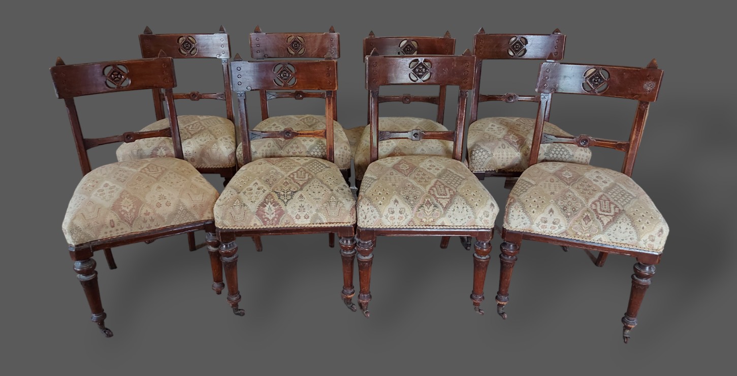 A set of eight Arts and Crafts dining chairs, each with a pierced carved rail back above a stuffover