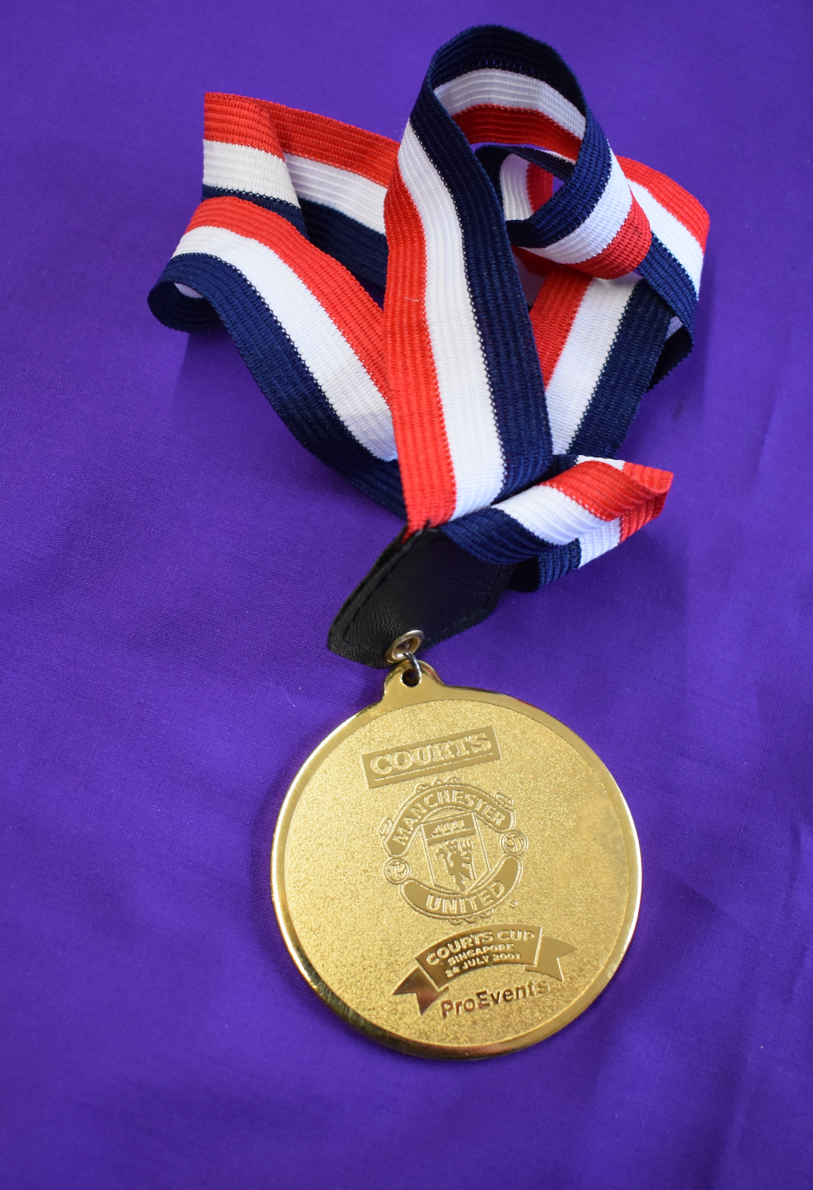 An engraved medal with red white and black ribbon presented to a Manchester United player on July