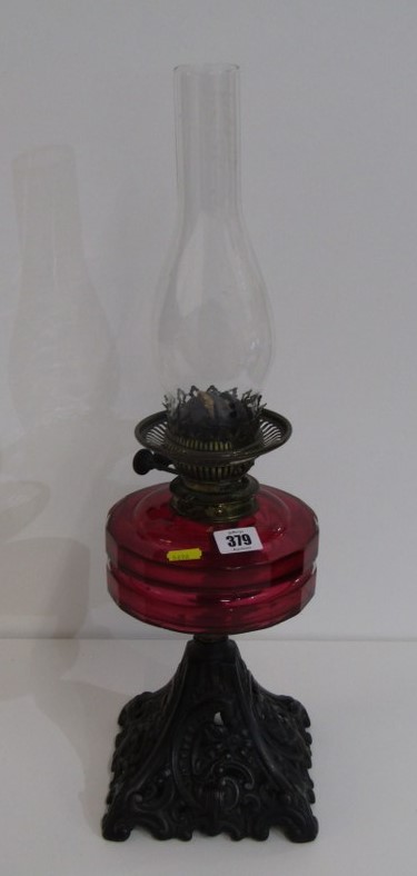 LATE VICTORIAN OIL LAMP, with cast iron foliate decorated base and red glass reservoir, 57cm