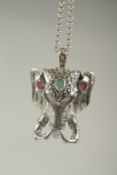 A silver elephant pendant set with ruby and emerald on a chain in a box.