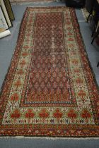 Early 20th century Persian long carpet, the central red ground field with stylised Boteh