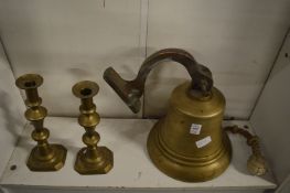 A large cast bronze bell and a pair of brass candlesticks.