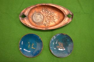 Copper dish inset with a coin together with a pair of enamel dishes.