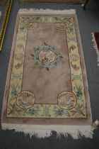 A Chinese rug, salmon pink ground with Chinese emblems 155cm x 92cm.