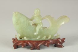A CHINESE CARVED JADE FIGURAL GROUP of a boy riding a giant fish, on a fitted carved hardwood stand,