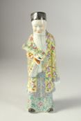 A CHINESE FAMILLE ROSE PORCELAIN FIGURE, the robe painted with peaches and longevity symbols, 27cm
