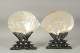 A PAIR OF CHINESE CARVED MOTHER OF PEARL SHELLS on fitted carved wood stands, each carved with