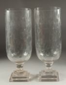 A PAIR OF CUT GLASS HURRICANE LAMPS on square stepped bases. 1ft 4ins high.
