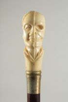 A CARVED BONE HANDLE WALKING STICK "HEAD & SKULL". 2ft 11ins long.