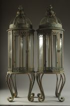 A LARGE PAIR OF METAL GLAZED LANTERNS on four curving legs. 33ins high.