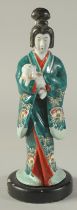 A JAPANESE KUTANI PORCELAIN FIGURE OF A GEISHA HOLDING A DOG, mounted to a wooden base, 31cm high