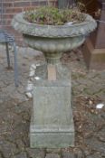 A reconstituted stone pedestal planter on square shaped base.