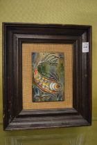 A wire work and enamel plaque depicting a fish, framed.