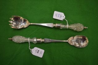 A pair of silver salad servers with cut glass handles.