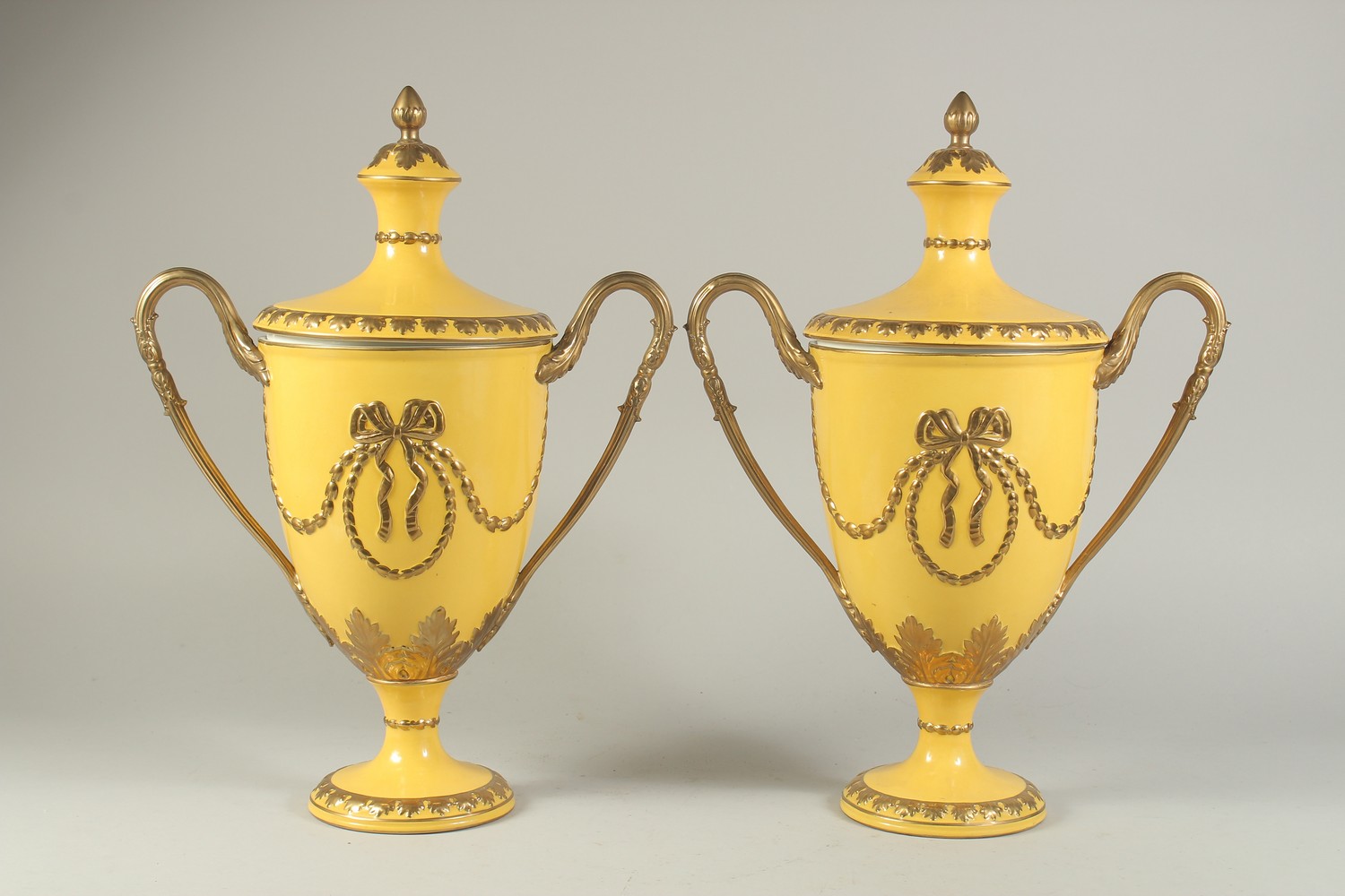 A PAIR OF SEVRES DESIGN YELLOW GROUND TWO-HANDLED URN SHAPED VASES AND COVERS. 17ins high.