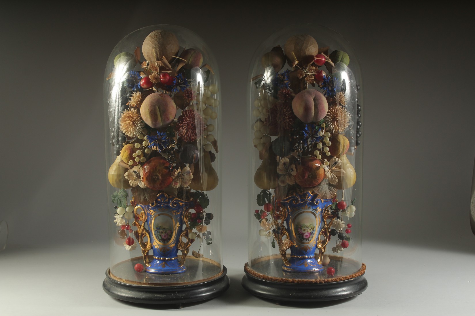 A VERY GOOD PAIR OF VICTORIAN GLASS DOMES, WAX FRUIT in a vase. 23ins overall.