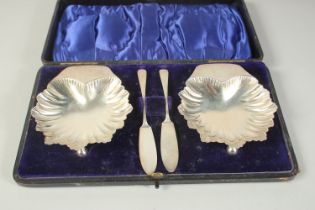 A PAIR OF SILVER SHELL SHAPE BUTTER DISHES AND KNIVES in a fitted case. London 1906.