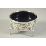 A GOOD LARGE SILVER CIRCULAR SALT with sapphire blue liner repousse side with cupids, supported on